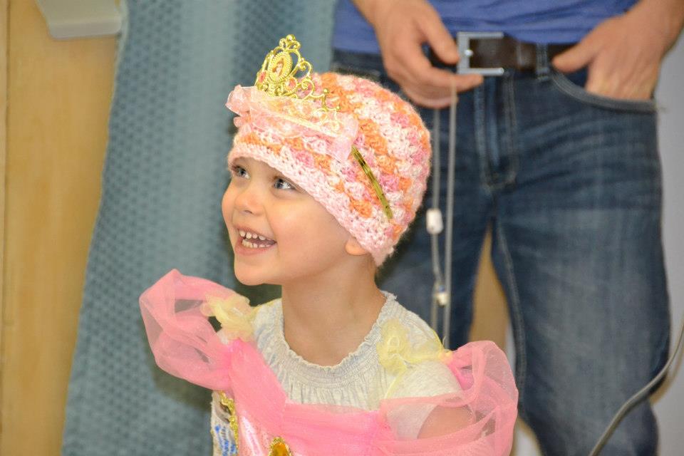 Une photo de Léa avec un sourire radieux et une jolie petite tuque qui dissimule son crâne nu suite aux traitements de chimiothérapie.